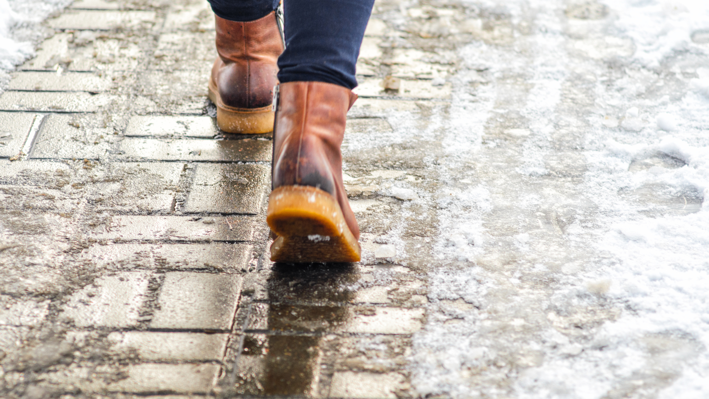 Close up of a half gritted walkway, with snow on the righthand side and a person walking on the left.